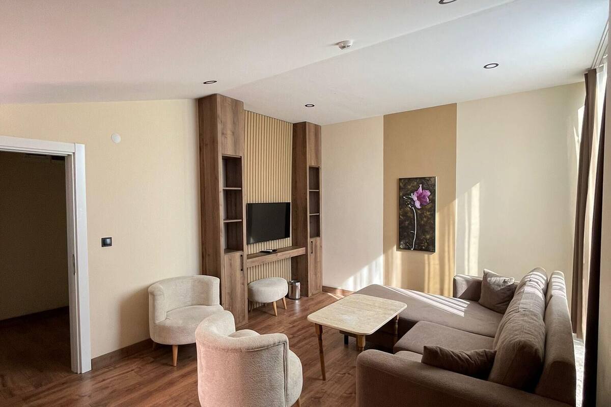 A modern living room with a sofa, armchairs, a coffee table, and a TV mounted on a wooden wall.
