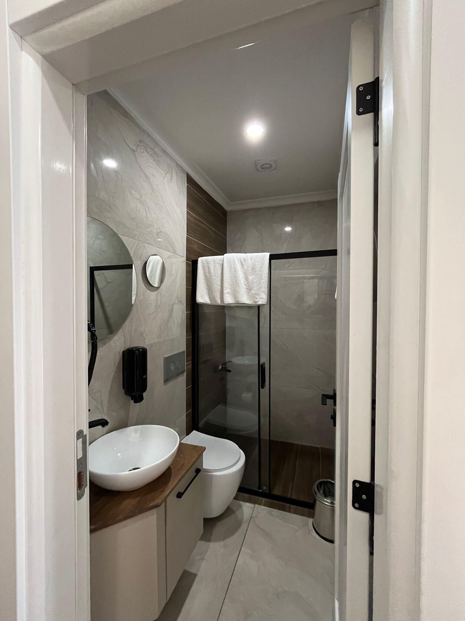 A modern bathroom with a marble vanity, a toilet, a glass shower enclosure, and a handheld showerhead.