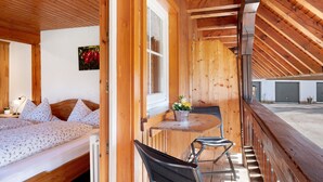 Una habitación de madera con una cama, un ventanal, una mesa con sillas y vista a un edificio.