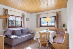 A cozy room with a wooden ceiling, a sofa, a dining table with chairs, and a bench.