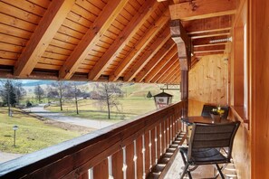 Un balcon en bois donnant sur une route et des collines.