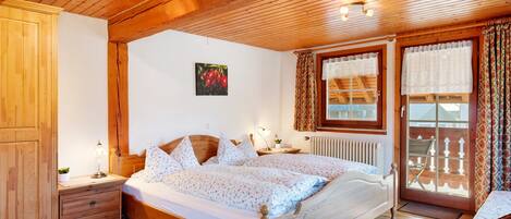 A wooden-paneled bedroom with a bed, bedside tables, and a view of the outside balcony.