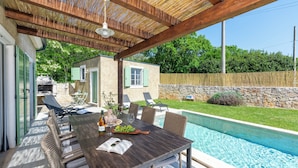 Un patio al aire libre con una mesa de madera, sillas y una piscina.