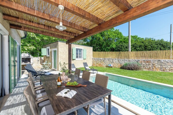 An outdoor patio with a wooden table, chairs, and a pool.