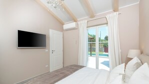 Un dormitorio con cama, televisor montado en la pared, una puerta y vistas al exterior.