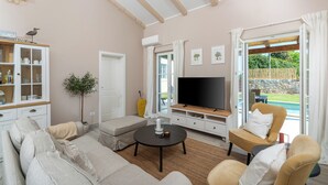 Una sala de estar con sofá, sillón, televisor y vista a una piscina.