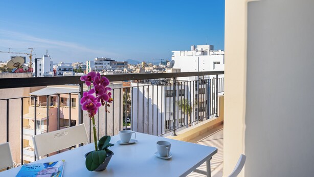 A balcony with a white table, two chairs, a vase with pink flowers, and a magazine. - Glade - 1 BR Apt. & Balcony in Larnaca (Larnaca)