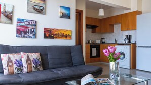 A modern living room with a grey sofa, a glass coffee table with a magazine, and a vase with flowers. - Glade - 1 BR Apt. & Balcony in Larnaca (Larnaca)