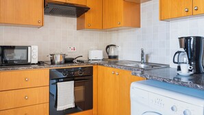 A kitchen with wooden cabinets, a stove, a microwave, a toaster, a coffee maker, and a washing machine. - Glade - 1 BR Apt. & Balcony in Larnaca (Larnaca)