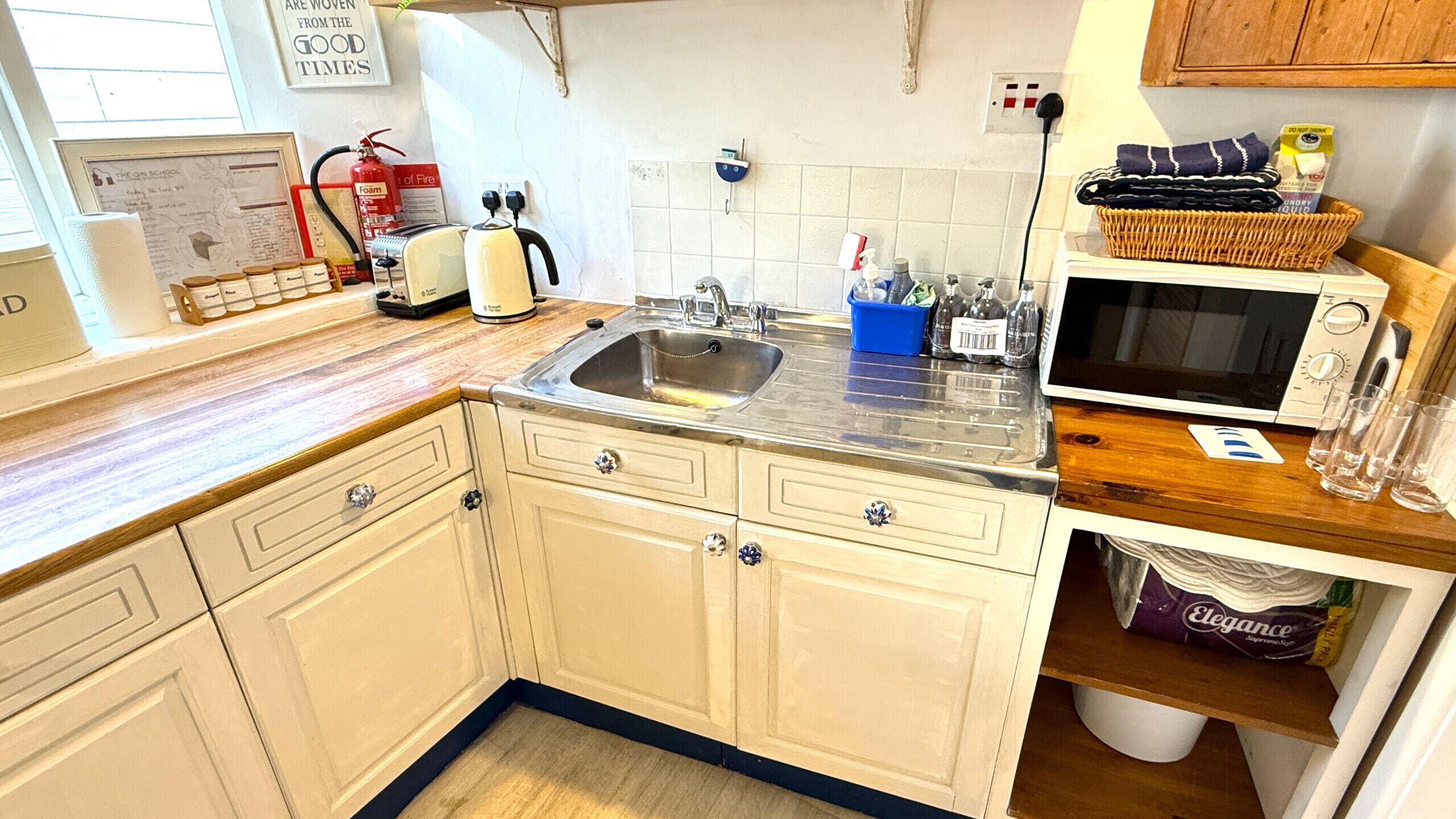 A kitchen with a sink, stove, microwave, and various appliances. There is a fire extinguisher, a fire hose, and a framed map on the wall.