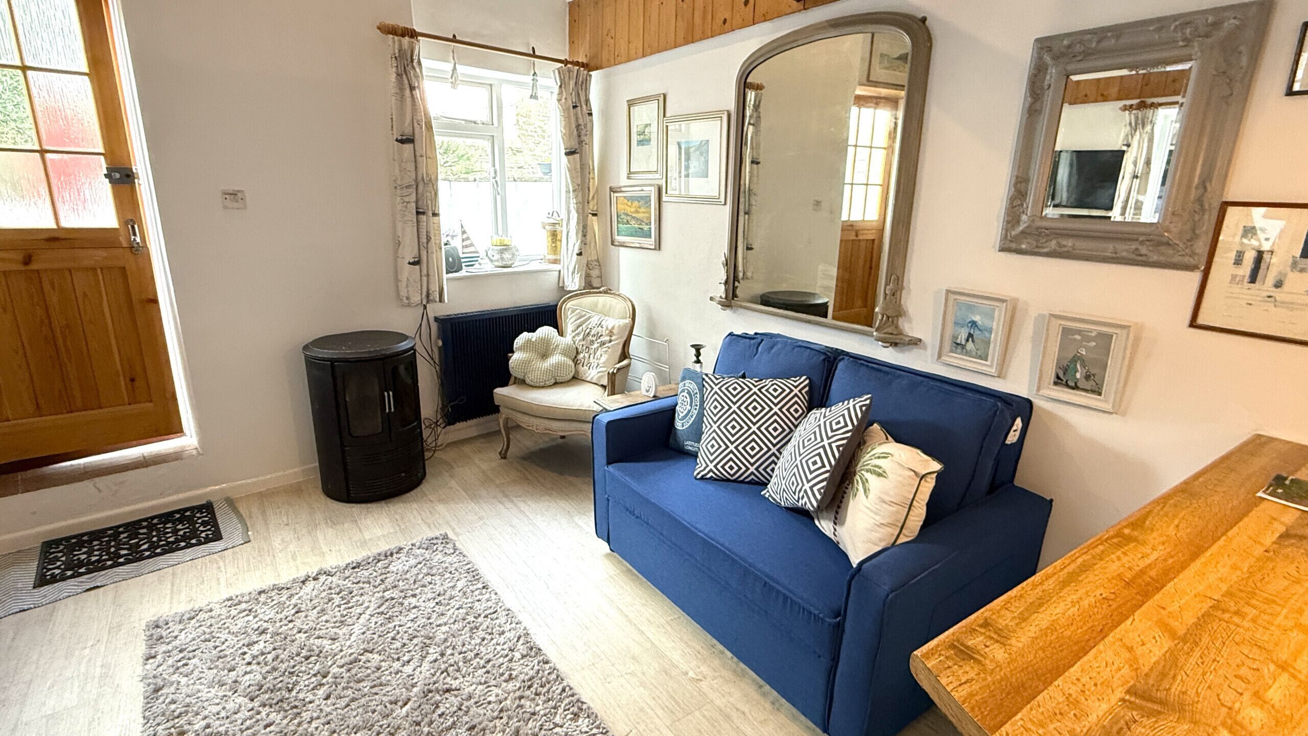 A cozy living room with a blue sofa, a wooden side table, a radiator, and a window with curtains.