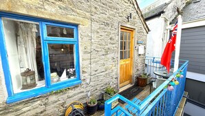 A stone building with a blue window and door, a small balcony with a red flag, and potted plants on the ground. - The Cabin in Salcombe (Salcombe)