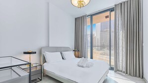 Een moderne hotelkamer met een groot bed, een glazen tafel en uitzicht op de stad door middel van kamerhoge ramen.