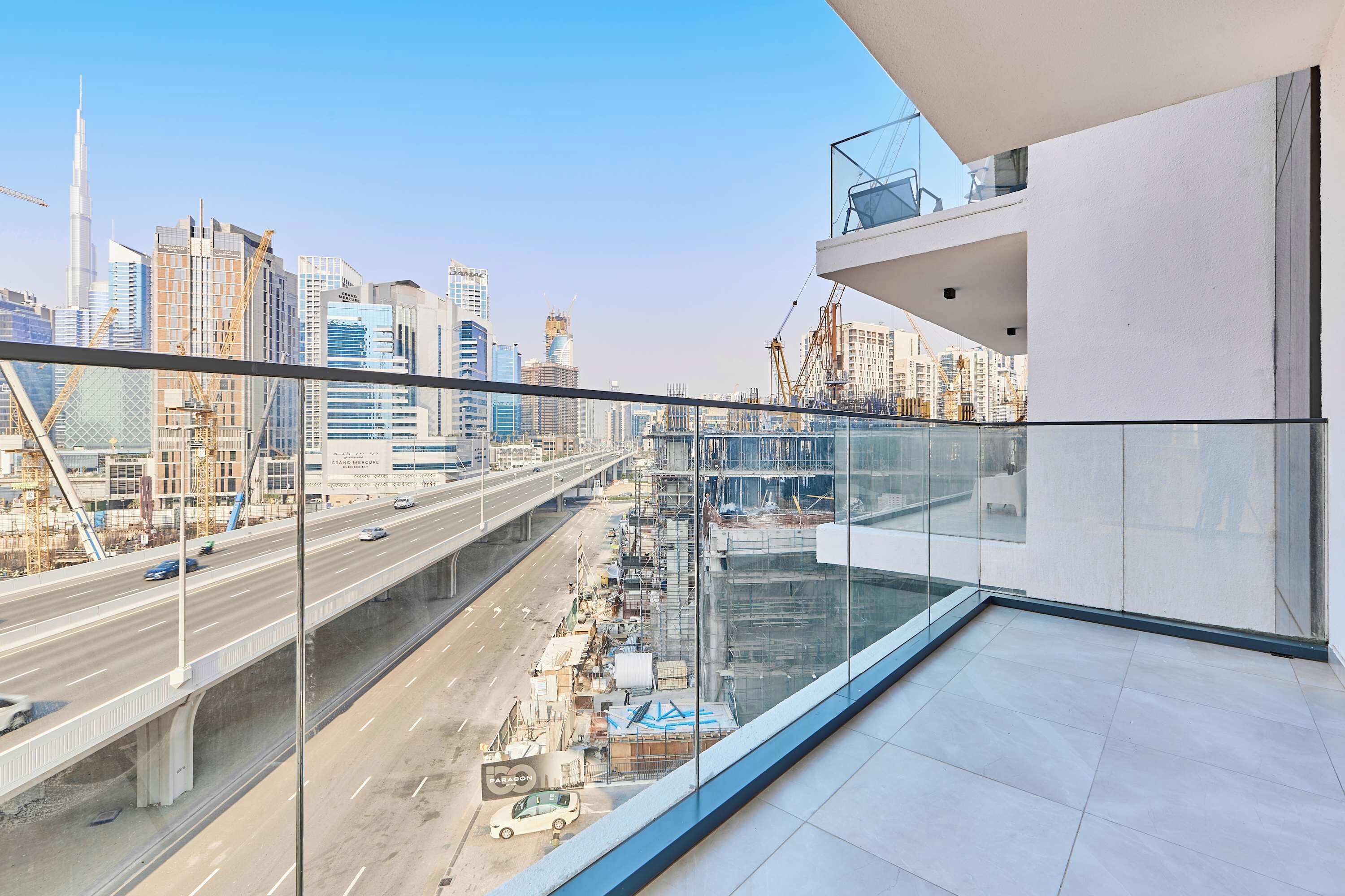 Un immeuble de grande hauteur doté d’un balcon en verre qui offre une vue panoramique sur la ville, avec ses nombreux gratte-ciel et une autoroute.