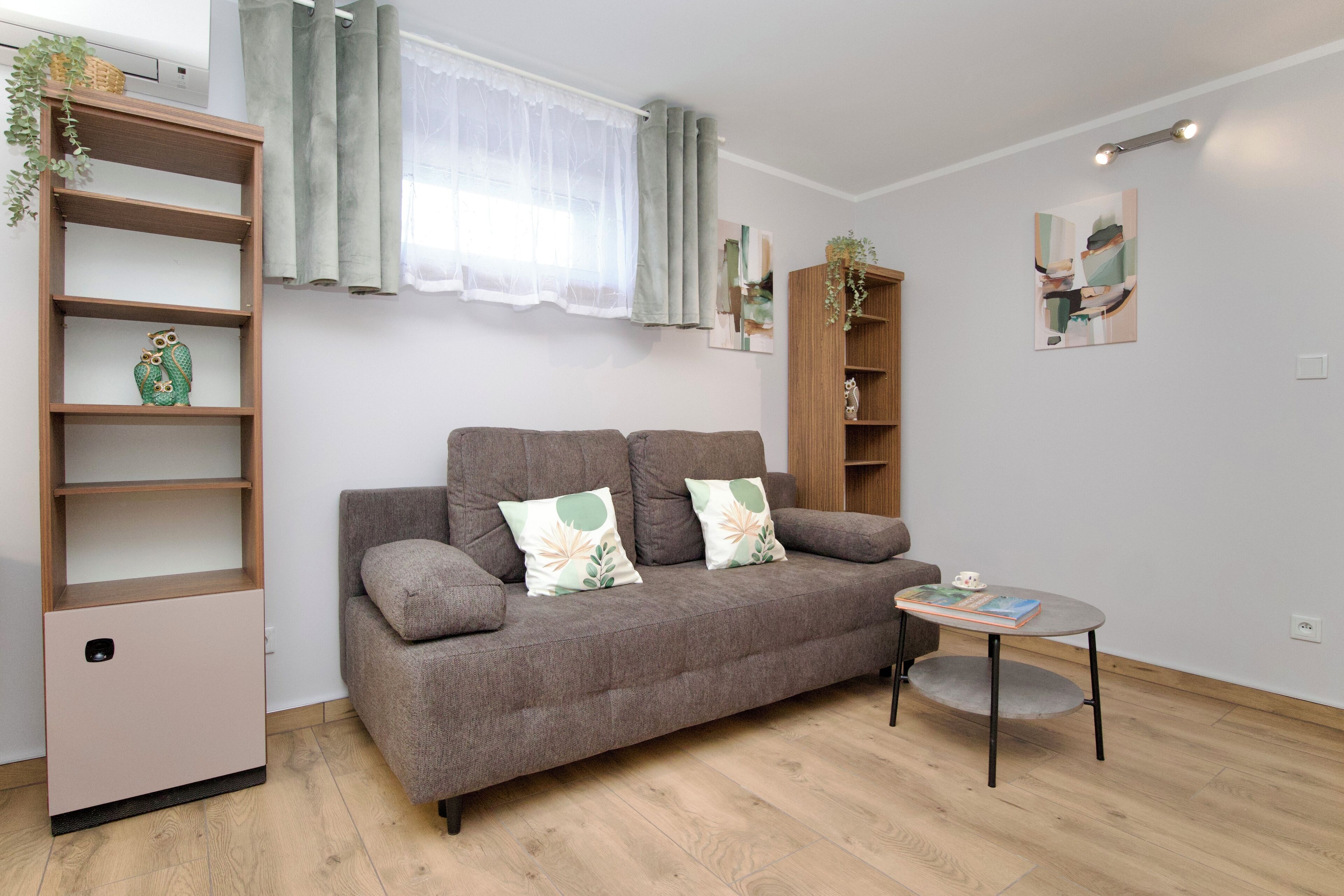A modern living room with a grey sofa, a small round table, and a wooden bookshelf.