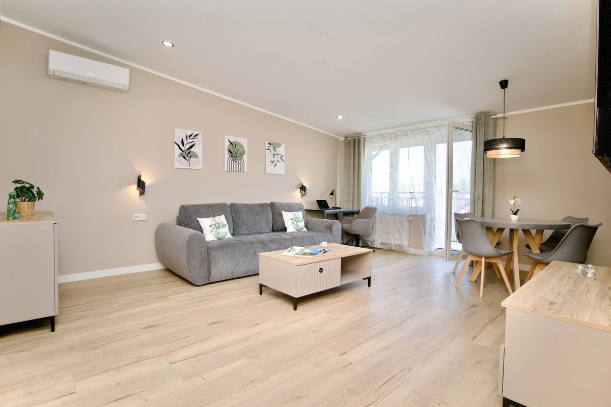 A modern living room with a grey sofa, a wooden coffee table, and a dining area with a table and chairs.