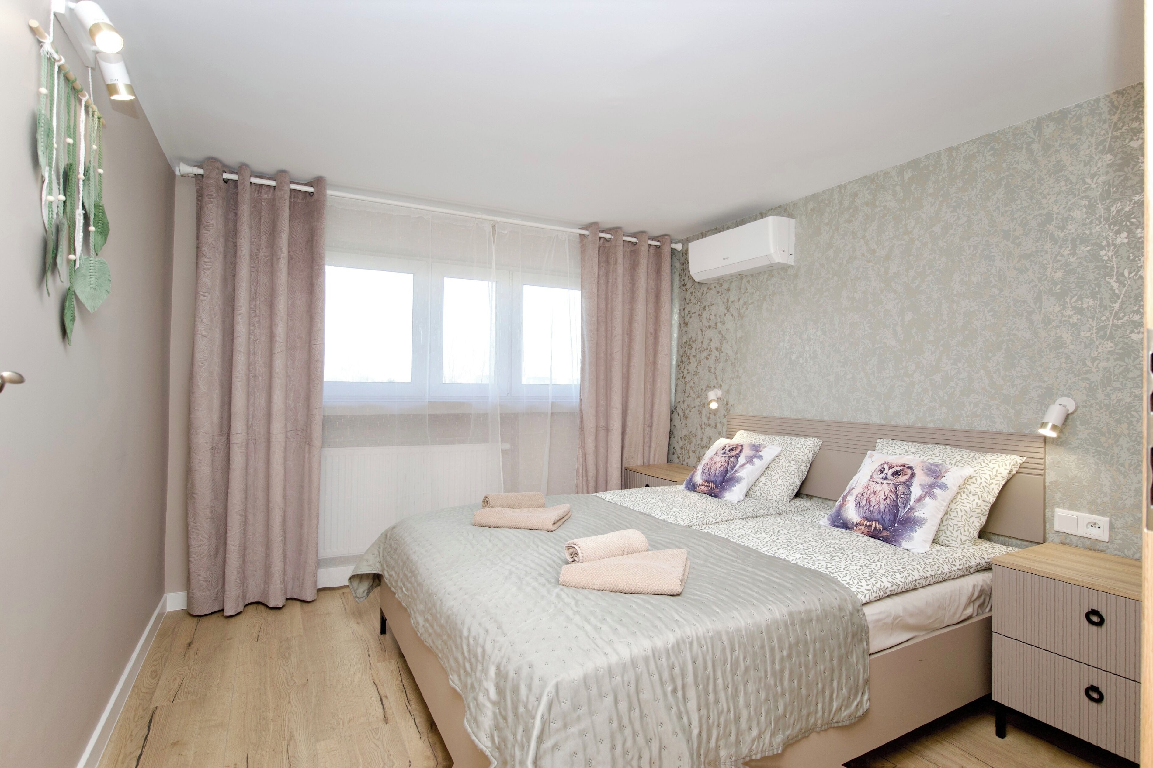 A bedroom with a bed, curtains, a bedside table, and a wall-mounted air conditioner.