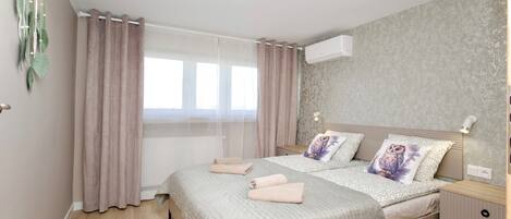 A bedroom with a bed, curtains, a bedside table, and a wall-mounted air conditioner.