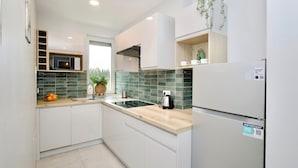 A modern kitchen with white cabinets, a built-in microwave, a kettle, and a refrigerator. - Łagiewniki Apartments Free Parking (Kraków)