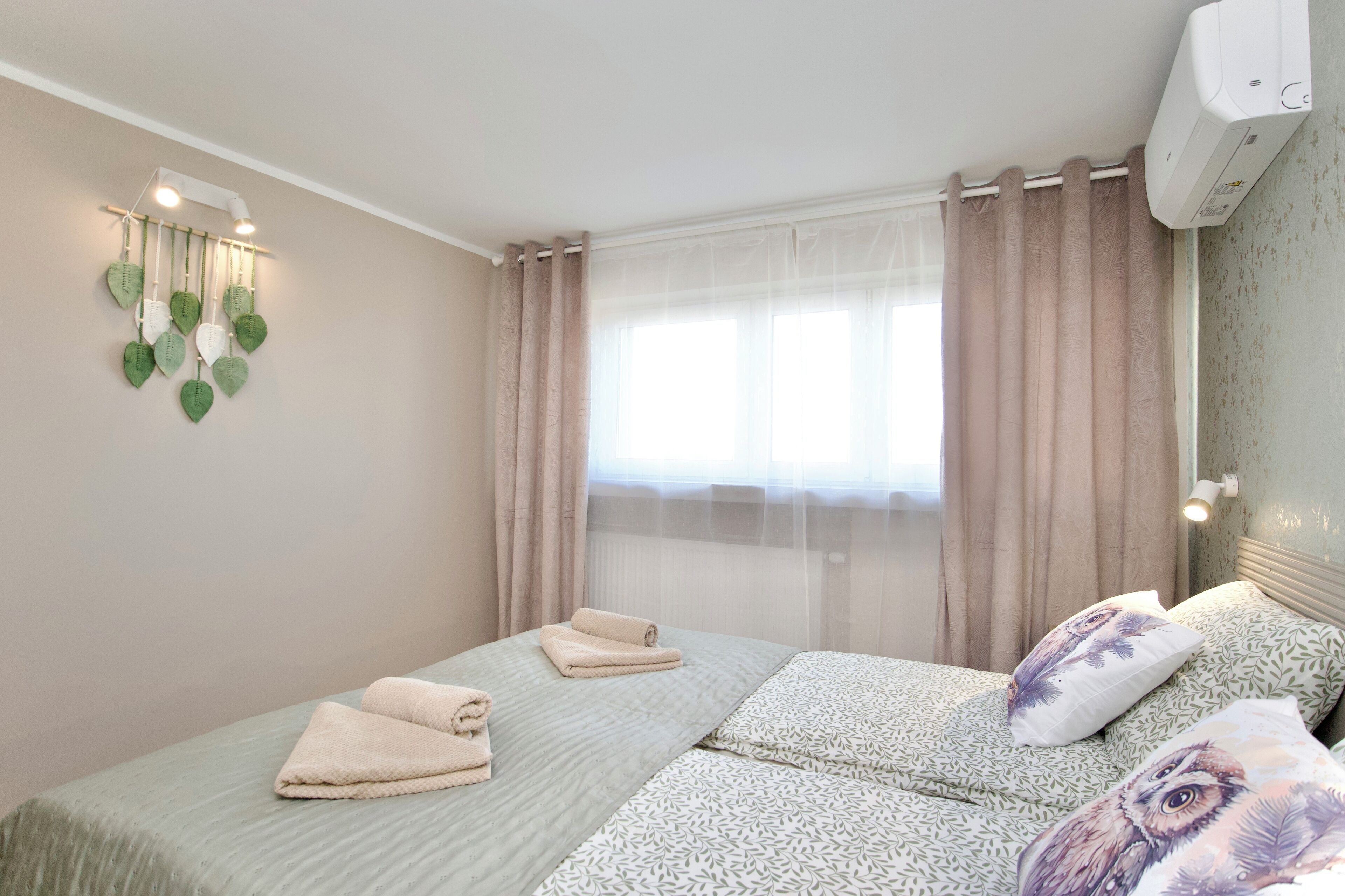 Une chambre avec deux lits, un luminaire fixé au mur et une fenêtre avec des rideaux.