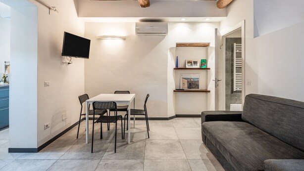 Ett modernt vardagsrum med ett vitt bord, svarta stolar, en grå soffa, en väggmonterad TV och en luftkonditioneringsanläggning.