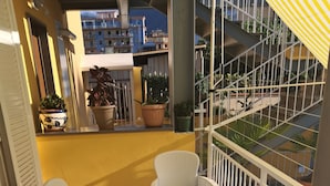 Un balcón con mobiliario de mimbre, plantas en macetas y vistas a edificios.