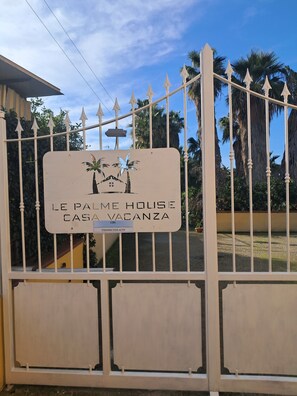 Een omheind eigendom met een bord waarop staat 'LE PALME HOUSE CASA VACANZA'.