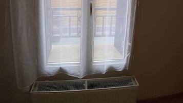 Huoneessa on suuri ikkuna, valkoinen patteri ja näkymä parvekkeelle, jossa on kaide.