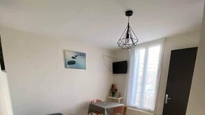 A small, well-lit room with a bed, a desk with a chair, a TV mounted on the wall, and a window with curtains. - Lena's townhouse (Saint-Denis)