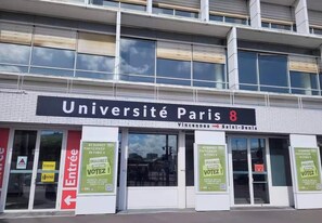 The exterior of Université Paris 8 with signage for 'Entrée' and 'Sortie' doors, and election posters on the windows. - Lena's townhouse (Saint-Denis)