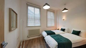 Une chambre avec deux lits, un radiateur, une fenêtre et un luminaire suspendu.