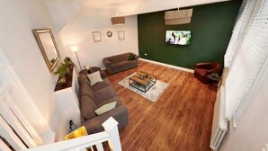 A living room with a sofa, armchairs, a coffee table, and a television on a green wall.