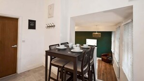 A dining area with a table set for four, a clock on the wall, and a door with a sign.