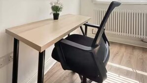 A room with a desk, chair, window with blinds, radiator, and a small plant.