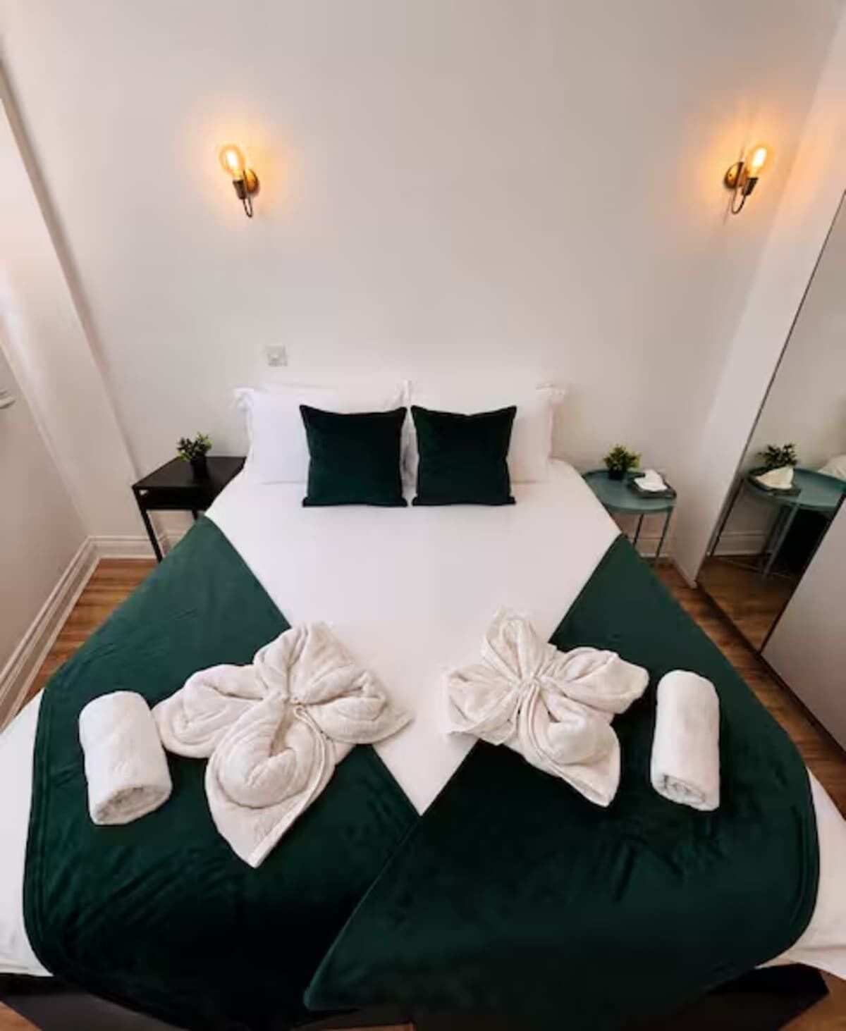 A hotel room with a bed, two nightstands, a mirror, and wall sconces.