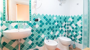 A bathroom with a sink, toilet, and bidet, tiled in a geometric pattern. - Domo Mea Rooms- Camera 1 (CABRAS)