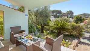 Un balcón con mobiliario de mimbre, una mesa de vidrio y vistas a una colina con árboles y edificios.