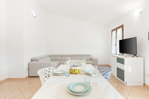 A dining area with a table set for four, a sofa, a television, and a laundry basket.