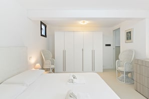 Ein Hotelzimmer mit einem Bett, zwei Korbstühlen, einem Schrank und einem gerahmten Bild an der Wand.