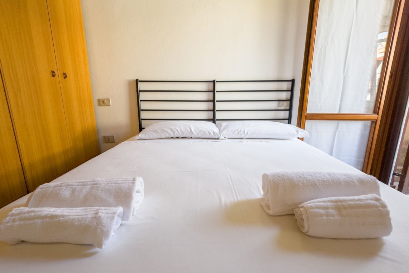 A hotel room with a bed, two towels, a wooden wardrobe, and a window.