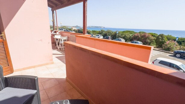 A balcony with a view of the sea, outdoor furniture, and parked cars.