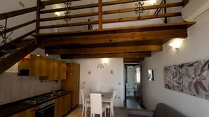 A kitchen with wooden cabinets, a dining table with chairs, a staircase with wooden beams, and a sofa.