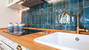 Una cucina dal design moderno, con piano cottura a induzione nero, lavello bianco con rubinetto dorato e schienale rivestito di piastrelle blu.