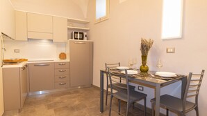 Een kleine keuken met een eettafel, stoelen, een magnetron en een vaas met gedroogde bloemen.