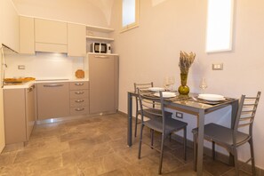 A compact kitchen with a dining table, chairs, a microwave, and a vase with dried flowers. - Residenza Deriu- Carmina (Bosa)