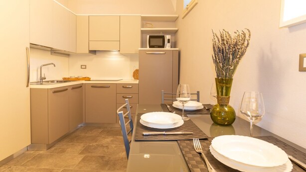 Een compacte keuken met een magnetron, een spoelbak en een eettafel gedekt voor twee personen, compleet met borden, bestek en een vaas met gedroogde bloemen.