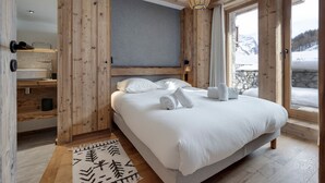 Une chambre avec un grand lit, des murs en bois, un mur d’accent de couleur grise, une commode en bois, un tapis blanc et une vue sur un paysage enneigé.