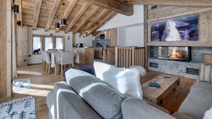 Un vaste espace de vie doté d’un haut plafond, de poutres en bois, d’une cheminée en pierre et d’un grand téléviseur fixé au-dessus.