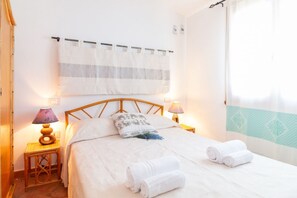 Ein Schlafzimmer mit einem Bett, zwei Nachttischlampen, einem Wandvorhang und einem Fenster mit Vorhang.