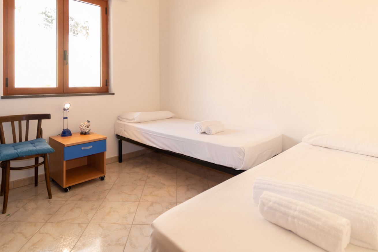 A bedroom with a single bed, a chair, a nightstand, and a window.